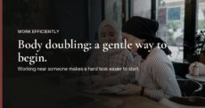 In a quiet, dimly lit cafe, two people sit close together at a wooden table, each writing in their own notebook, over the words "Body doubling: a gentle way to begin."